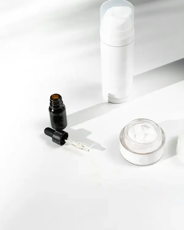 Frasco pump branco, frasco conta-gotas e pote de creme sobre mesa clara
