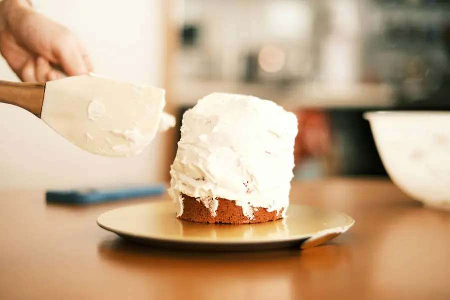 Mãos cobrindo um bolo com creme usando uma espátula