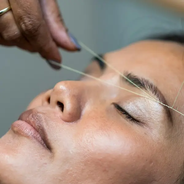 Profissional modela a sobrancelha da cliente com linha