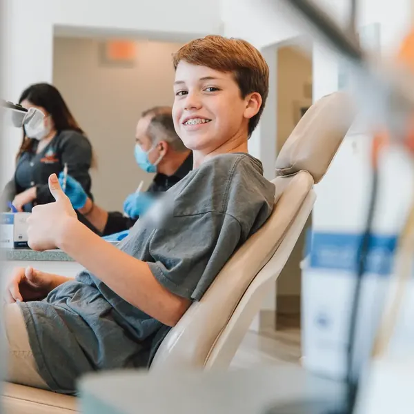 Menino sentado na cadeira do dentista faz sinal de positivo