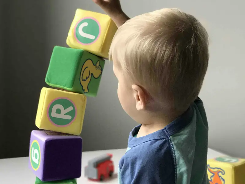Criança pequena, de costas, empilhando cubos coloridos