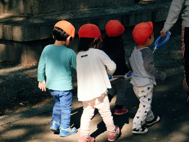 Crianças de boné vermelho caminhando juntas com a educadora