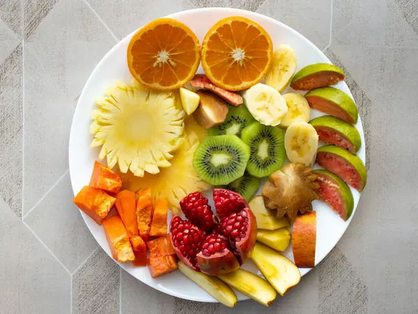 Prato com frutas cortadas: laranja, kiwi, abacaxi e romã