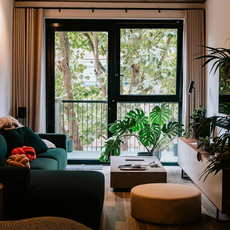 Sala de apartamento com sofá verde, plantas e porta de vidro para a varanda