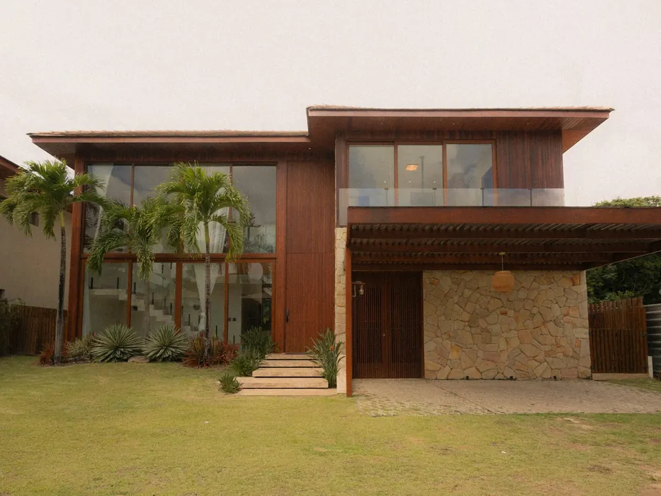 Fachada da Casa Pajuçara, com madeira, pedra e palmeiras no jardim